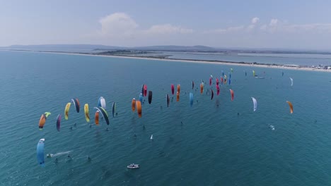big-group-of-kitesurfers-racing,-view-by-drone.-Sunny-day-coastline